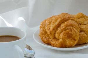 croissant de manteiga e uma xícara de café no café da manhã foto