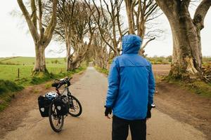 bicicleta de passeio montada com cestos. sebes escuras na Irlanda do Norte. viajante masculino fica de bicicleta visita marcos famosos na irlanda do norte foto
