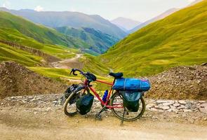bicicleta de turismo vermelha carregada com acessórios fica nas montanhas do cáucaso com belo panorama da estrada foto