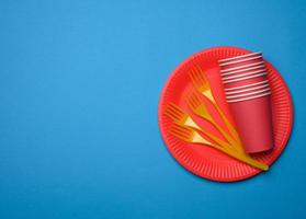 garfos de plástico laranja e pratos descartáveis de papel vermelho vazio em um fundo azul foto