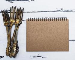 caderno com páginas vazias marrons e uma pilha de garfos de metal foto