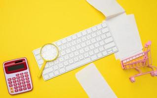 teclado sem fio branco, pilha de recibos de papel e lupa em fundo amarelo, conceito de análise de orçamento foto