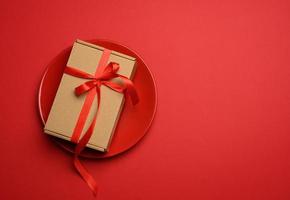 caixa de papelão marrom retangular amarrada com uma fita vermelha de seda encontra-se em uma placa redonda de cerâmica vermelha foto