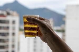 homem segurando copo de cerveja no fundo desfocado da cidade urbana foto