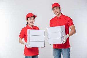 imagem de um jovem entregador feliz em uniforme de camiseta em branco de boné vermelho em pé com caixa de papelão branca vazia isolada no estúdio de fundo cinza claro foto