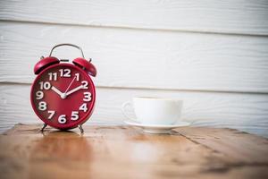 despertador vermelho com café na mesa de madeira foto