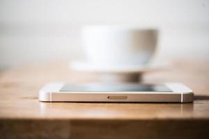 uma xícara de café e smartphone na mesa de madeira no café foto