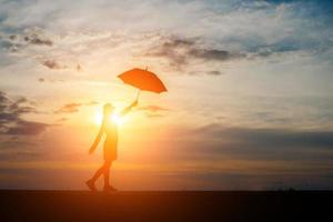 silhueta de uma mulher segurando um guarda-chuva na praia e no pôr do sol foto