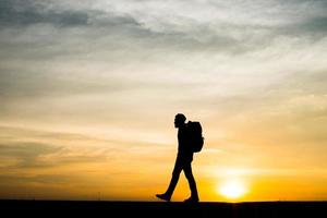 silhueta de um jovem mochileiro caminhando durante o pôr do sol foto
