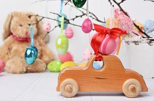 carro de brinquedo de madeira carregando um ovo de páscoa rosa fixado com uma fita vermelha foto