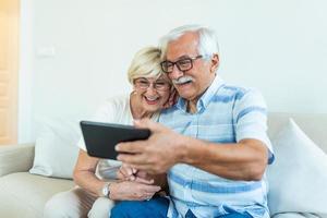 idosos alegres navegando na internet com tablet, família, tecnologia, idade e conceito de pessoas - casal sênior feliz com computador tablet pc em casa foto