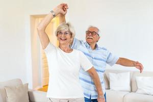 casal romântico aposentado alegre e ativo dançando rindo na sala de estar, feliz esposa de meia idade e marido mais velho se divertindo em casa, sorrindo avós da família sênior relaxando se unindo foto