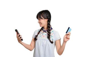 retrato da bela jovem mulher asiática feliz em vestido jeans segurando o cartão de crédito e smartphone em fundo branco. tiro de estúdio foto