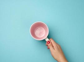 mão feminina segura uma caneca de cerâmica em um fundo azul, pausa e toma café foto