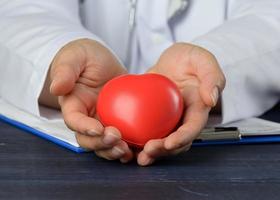 médico dentro uma branco casaco segurando uma vermelho coração. órgão doação conceito, sangue doação foto