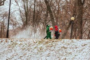 dnepropetrovsk, ucrânia - 02.04.2022 trabalho sazonal de serviços públicos da cidade no parque. um trabalhador com um soprador de mochila motorizado sopra neve de um caminho do parque. foto