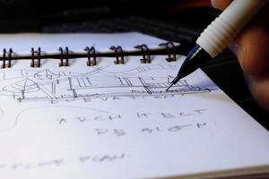 as mãos do arquiteto estão esboçando planos arquitetônicos com lápis em um caderno em uma mesa com um laptop. foto