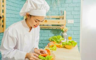 mulher asiática com uniforme de chef está cozinhando na cozinha. foto