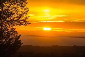 caloroso pôr do sol com nuvens árvore e poder linhas foto