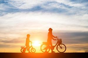 mãe com seu filho andando de bicicleta ao pôr do sol foto