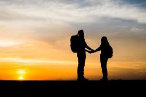 silhuetas de dois caminhantes com mochilas apreciando o pôr do sol foto