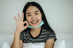 garota usando máscara higiênica, camisa listrada e símbolo de mão ok