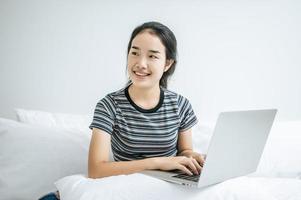 uma jovem brincando em seu laptop na cama foto