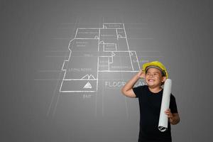 um menino usando um chapéu amarelo de engenheiro e uma planta da casa no quadro-negro foto