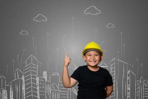 menino usando um chapéu amarelo de engenheiro e idéias de planos de casa no quadro-negro foto