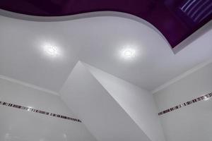 detalhe do teto de canto com intrincado trabalho de estuque. teto falso e drywall com lâmpadas halógenas em sala em apartamento ou casa. esticar teto roxo de forma complexa. foto