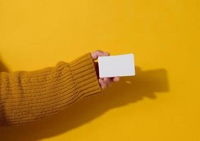 fêmea mão segurando esvaziar papel branco o negócio cartão em uma amarelo fundo. cópia de espaço foto