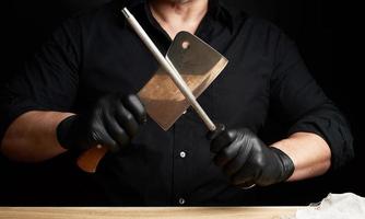 chefe de cozinha dentro uma Preto camisa e Preto látex luvas aguçar uma cozinha faca em a ferro apontador com uma lidar com foto