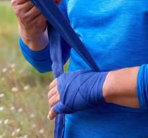 atleta ficar de pé e embrulho dele mãos dentro azul têxtil elástico curativo antes Treinamento foto