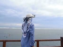 costas da mulher de chapéu na praia tropical que olhava o céu e o mar da ponte. vista do mar foto