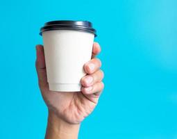 mão de homem segurando uma xícara de café branco, cheia de café preto quente americano, sem açúcar sem leite, pronto para beber, refrescante. aroma acordado fresco para trabalhar colocado em um fundo azul isolado foto