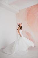 jovem noiva dentro branco vestir com flor guirlanda em dela cabeça dançando dentro a estúdio foto