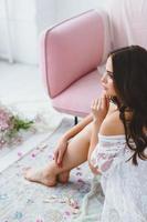 jovem noiva dentro branco lingerie posando perto a rosa sofá dentro a estúdio foto