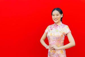 lindo ásia mulher com grandes cabelo quem desgasta Rosa cheongsam vestir dentro chinês Novo ano tema enquanto ela mostra dela mão Como chinês cumprimento com em vermelho fundo. foto