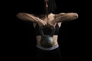 linda garota atlética com cabelo preto levantado com as duas mãos um peso de metal foto