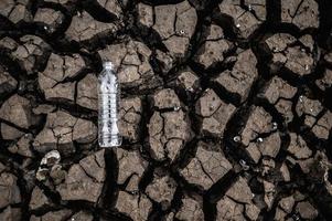 garrafa de água em solo seco com terra seca foto