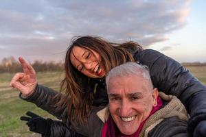 meio envelhecido casal vestindo inverno roupas levando uma selfie dentro a campo foto