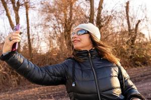 meio envelhecido mulher vestindo inverno roupas levando uma selfie de uma rio foto