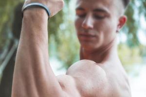 jovem muscular adulto mostrando fora dele bíceps ao ar livre foto
