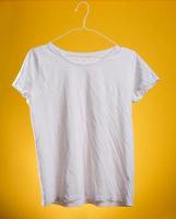 branco algodão amassado camiseta suspensão em uma cabide em uma amarelo fundo, verão roupas foto