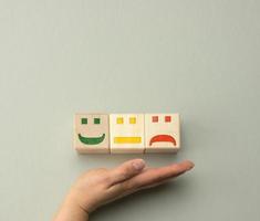 blocos de madeira com emoções diferentes do sorriso à tristeza e a mão de uma mulher. conceito para avaliar a qualidade de um produto ou serviço foto