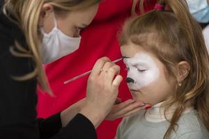 uma Maquiagem artista desenha face pintura em a face do uma pequeno garota. foto