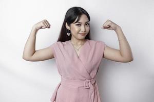 animado ásia mulher vestindo uma Rosa blusa mostrando Forte gesto de elevação dela braços e músculos sorridente orgulhosamente foto