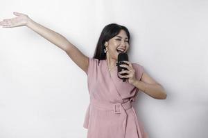 retrato de mulher asiática despreocupada, se divertindo karaokê, cantando no microfone em pé sobre fundo branco foto