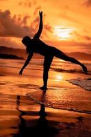 silhueta do a ásia mulher dançando balé com ótimo flexibilidade e uma Visão do a ondas atrás dela foto