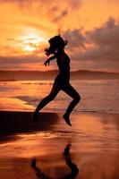 silhueta do a ásia mulher praticando dela balé movimentos em a de praia com a ondas falhando antes a festival começa foto